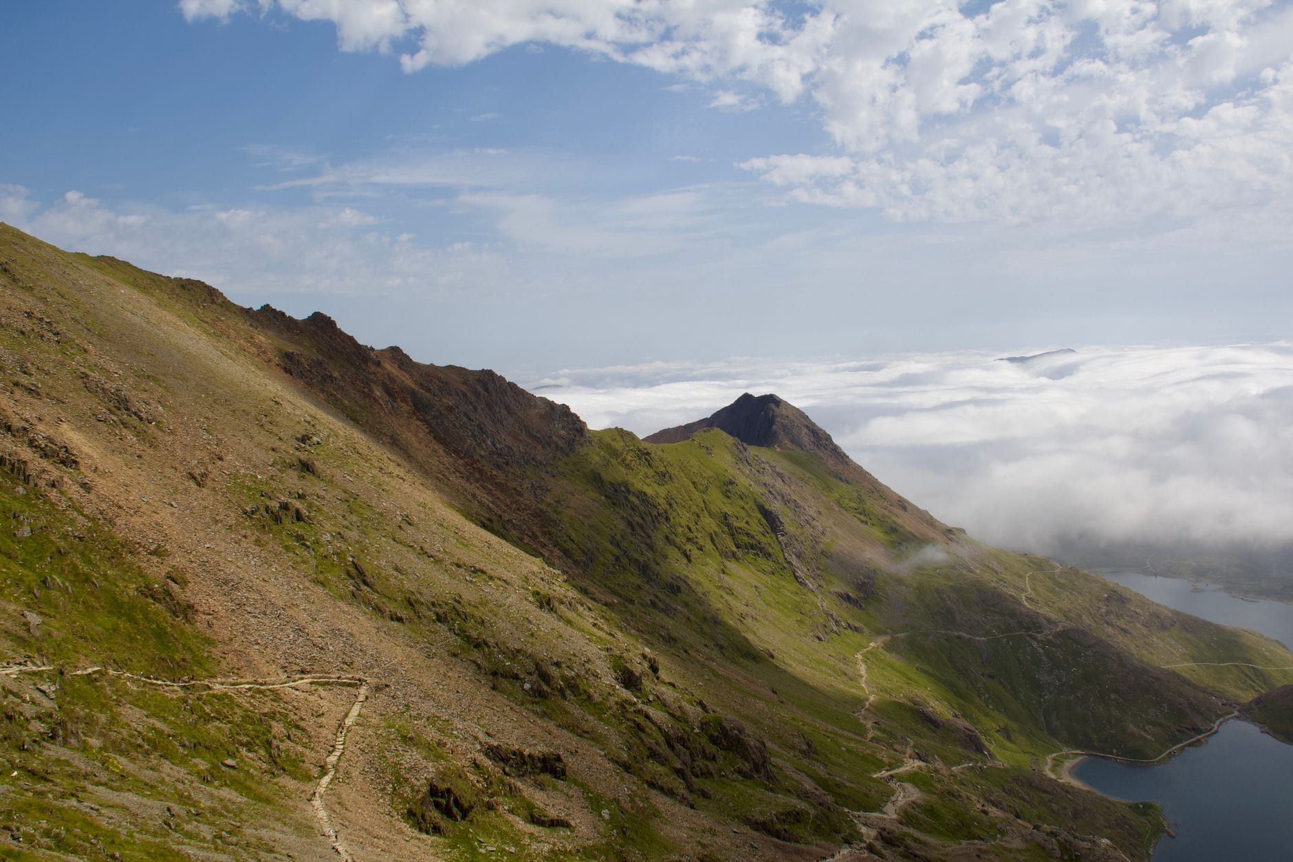 Des crêtes montagneuses escarpées et des sentiers sinueux s'élèvent au-dessus de nuages bas et d'un lac au Pays de Snowdonia.