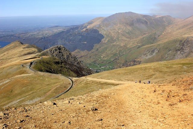 Des randonneurs marchent sur le sentier de Llanberis le long de la voie du chemin de fer de la montagne de Snowdon serpentant dans les montagnes du Pays de Snowdonia.