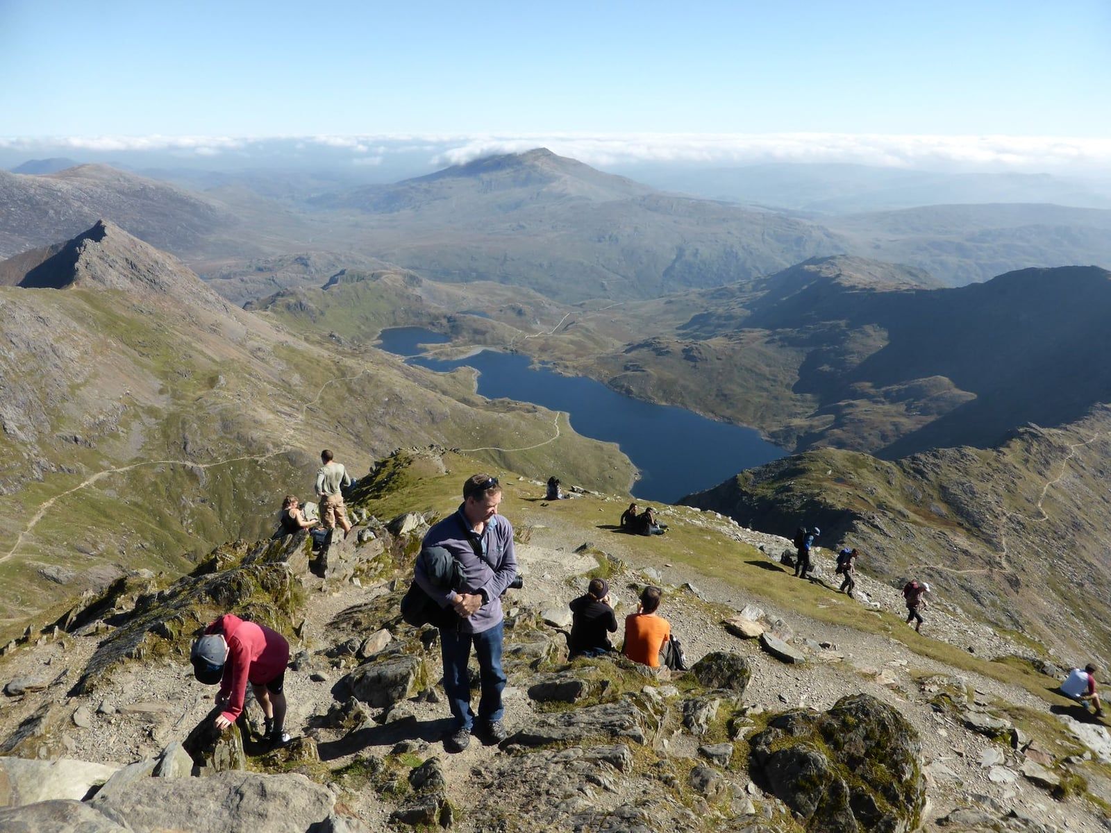 Des randonneurs se reposent au sommet rocheux du Snowdon, surplombant Llyn Llydaw et les massifs montagneux environnants de Snowdonia.