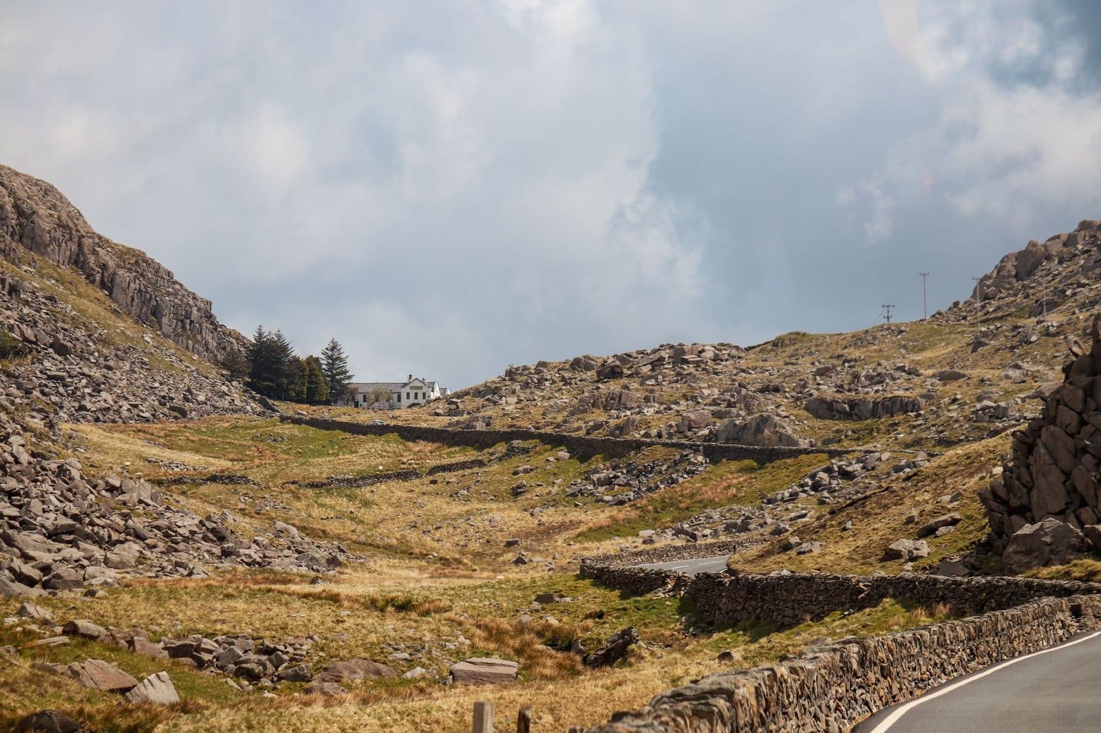 Een kronkelende weg met droge stenen muren stijgt op door het rotsachtige landschap van de Llanberis Pass in Snowdonia.