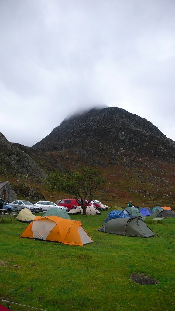 Zelte auf einer grünen Campingwiese unter einem wolkenbekränzten Berggipfel in Snowdonia.