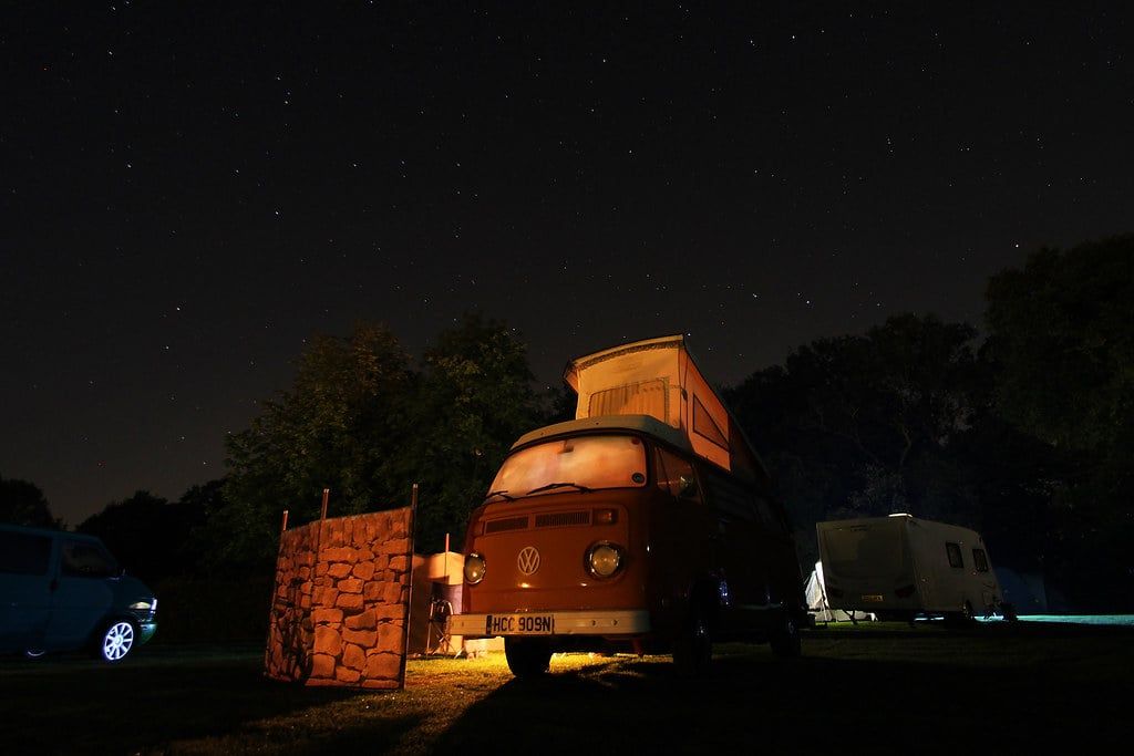 Ein Vintage-Volkswagen-Campervan in Rot mit beleuchtetem Klappdach unter einem Sternenhimmel auf einem Campingplatz in Snowdonia.