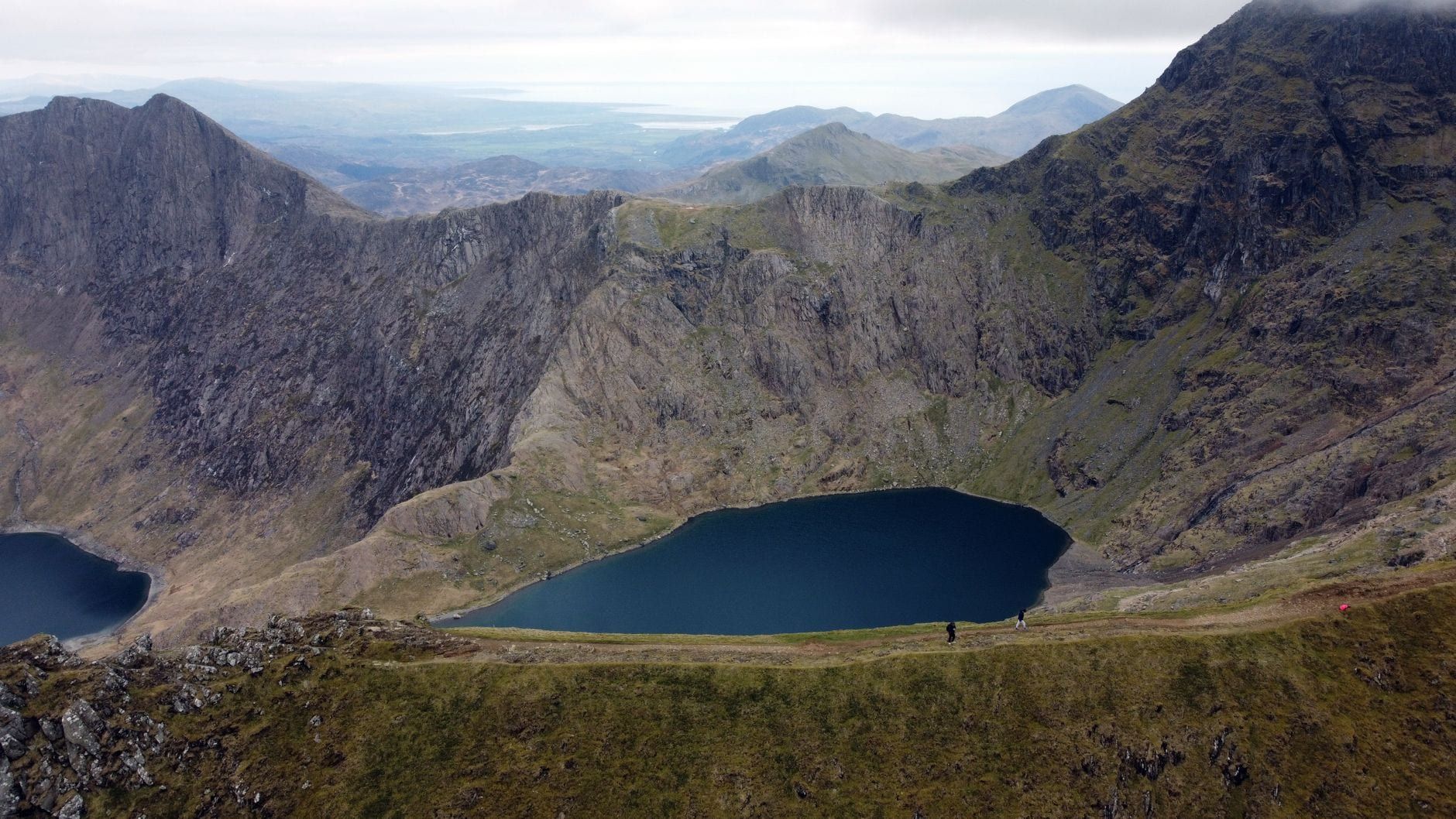 Des randonneurs marchent le long d'une haute crête surplombant un lac glaciaire d'un bleu profond dans le Snowdonia.