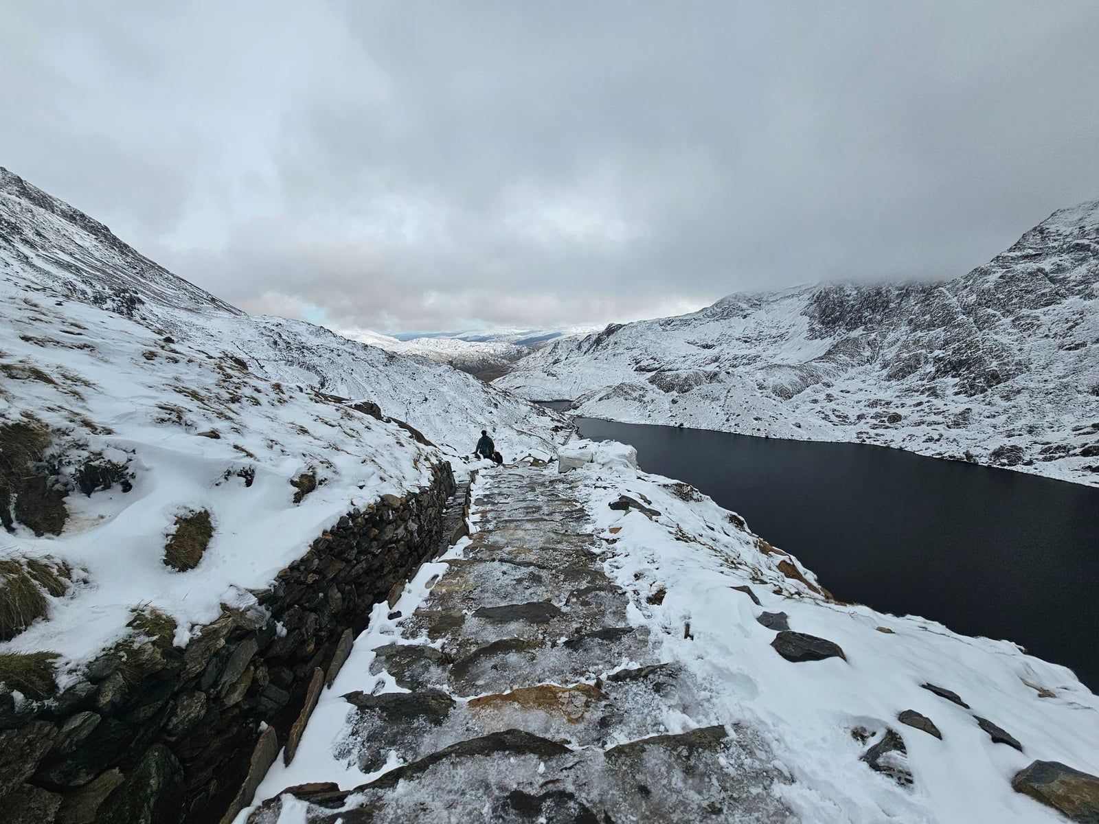 A snow-covered stone staircase on the Pyg Track overlooks Llyn Llydaw in Snowdonia.