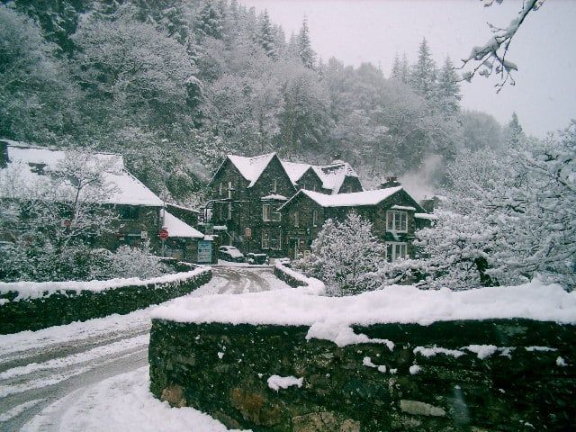 Snow blankets the stone bridge and traditional buildings of Betws-y-Coed in Snowdonia.