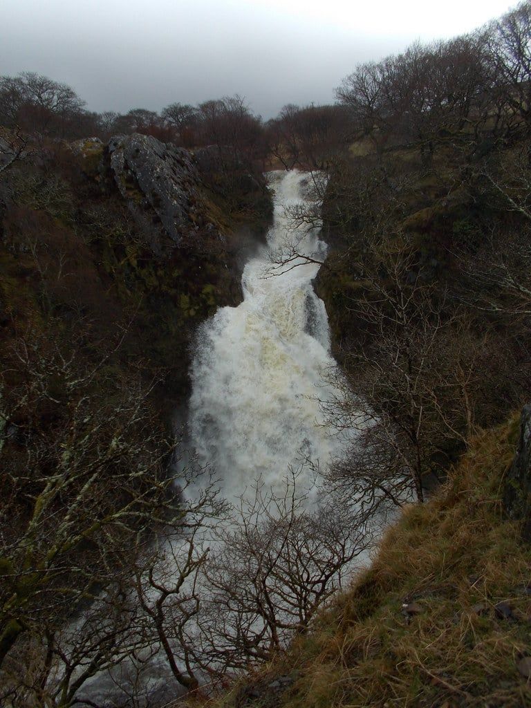 Ceunant Mawr waterfall in Snowdonia cascades in full flow down a rocky, wooded gorge near Llanberis.