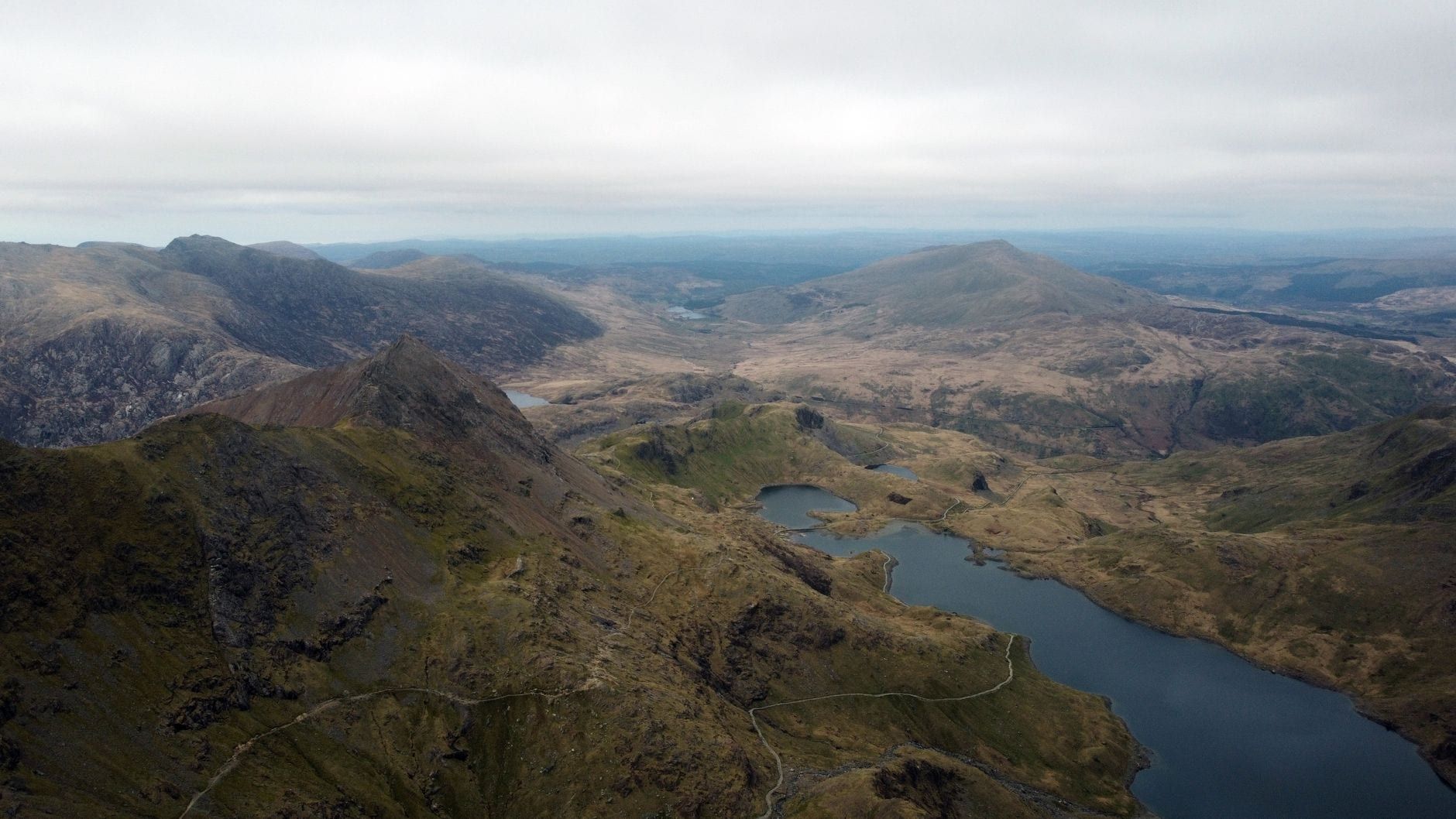 Panoramische Luftaufnahme über schroffe Berggipfel und Gletscherseen im Snowdonia-Nationalpark bei bedecktem Himmel.